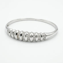 Load image into Gallery viewer, A polished silver bangle bracelet featuring a decorative front band with textured metallic segments and rows of small clear pavé stones, shown on a plain white background.
